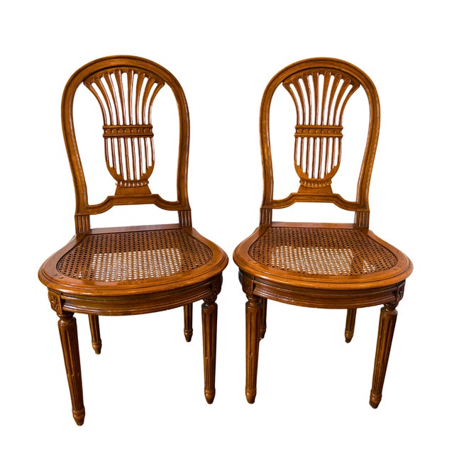 Elegant pair of French Louis XVI style chairs featuring finely carved lyre-shaped backs and hand-caned seats. Crafted in...