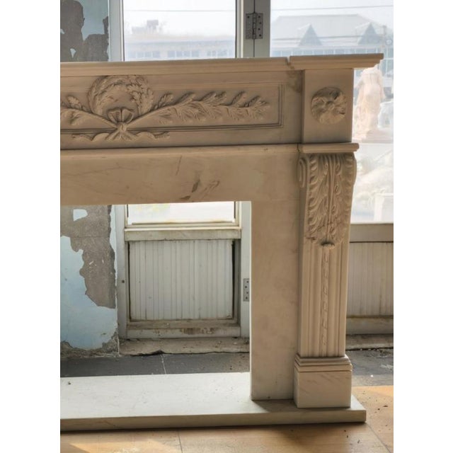 Elegant and understated, this neoclassical-style fireplace mantle is crafted from smooth white marble with subtle veining...