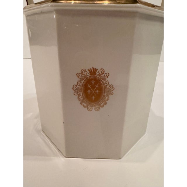 Elegant white and gold diminutive ice bucket with regal crest decoration and gold finial. With handle up, 13” h. Down 12”...