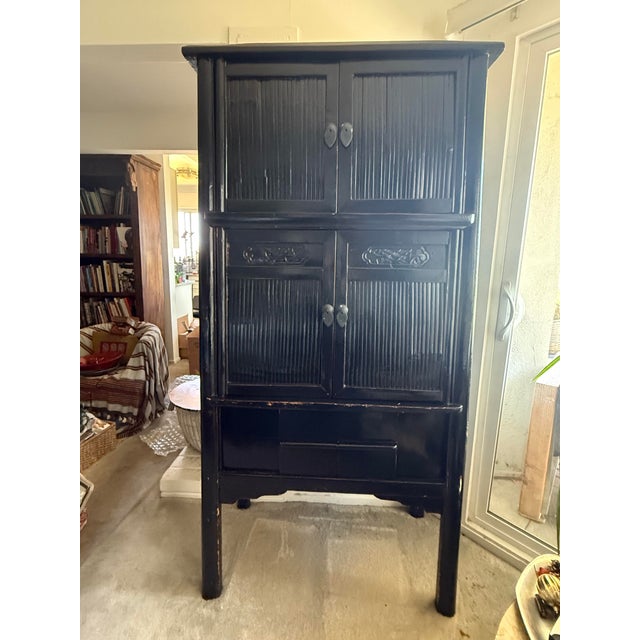 A tall 2 piece stacking cabinet finished in black lacquer featuring vertical bamboo slat panels on the upper and lower...