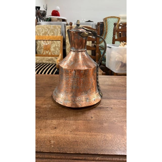 An authentic antique handcrafted copper pitcher featuring a heavily textured hand-hammered finish with aged patina and...
