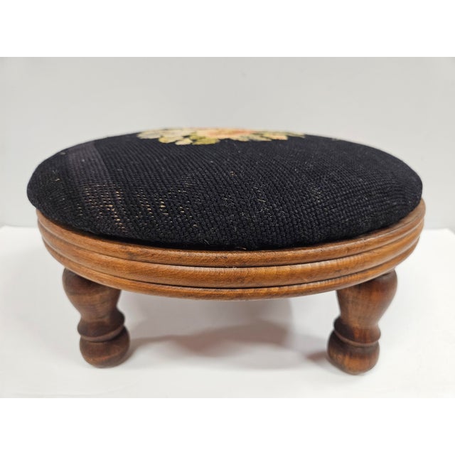 This Victorian style round needlepoint footstool features a floral motif against black background. The base of the stool...