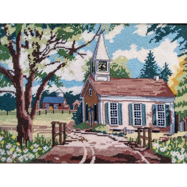 This 1970s framed vintage needlepoint depicts a country scene featuring a church with a steeple, tree and lane in the...