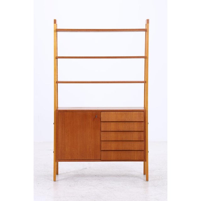 Vintage teak shelving unit with a slim, lightweight design and integrated storage. The upper section features three open...