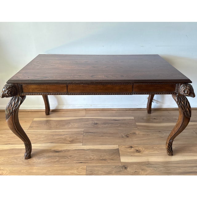 An early 20th-century mahogany writing desk or console table, featuring exquisitely carved ram’s head motifs at each...