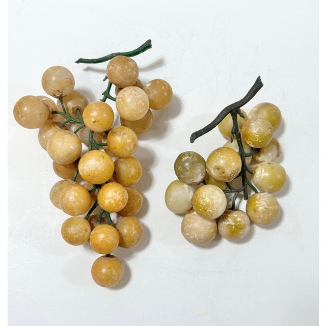 Two alabaster grape clusters in golden yellow, cream and muted green tones with branching green stems. The clusters differ...