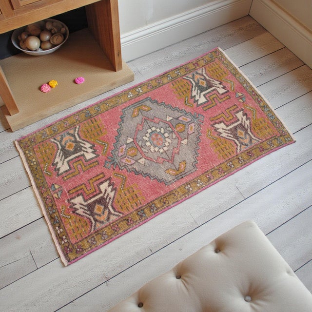 This charming vintage Nigde rug features a soft, sun-faded pink field adorned with striking geometric medallions and...