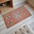 This charming vintage Nigde rug features a soft, sun-faded pink field adorned with striking geometric medallions and...