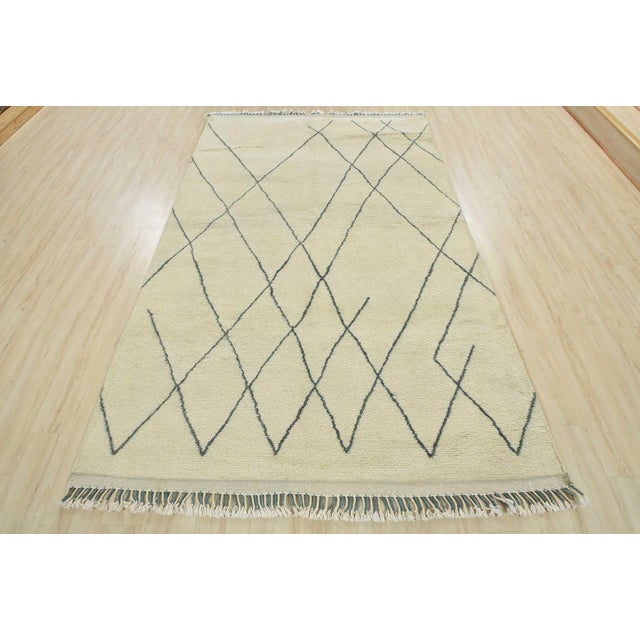 A contemporary Moroccan rug hand-knotted with an all-wool pile on a cotton foundation. This area rug features an all-over...