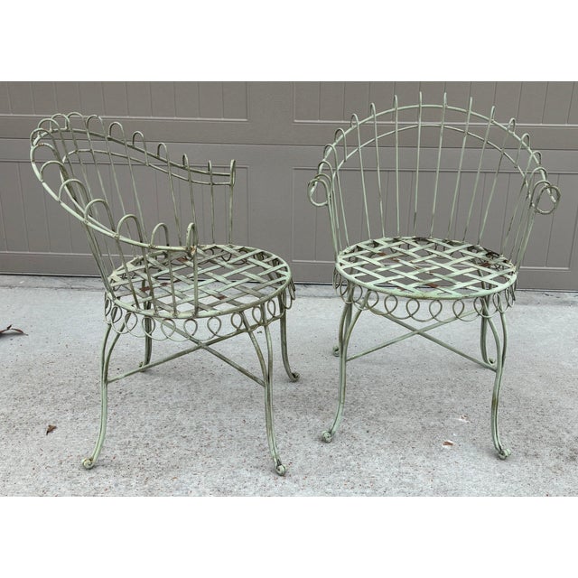 A charming pair of vintage French wrought iron garden chairs featuring round lattice strap-iron seats and elegantly curved...