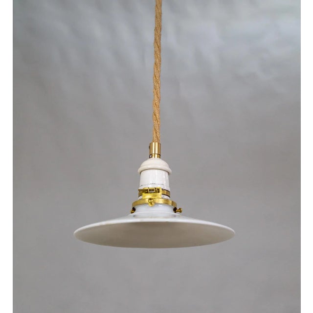 A contemporary pendant light with a rope-covered cord, small milk glass saucer shade, and ceramic and brass canopy....