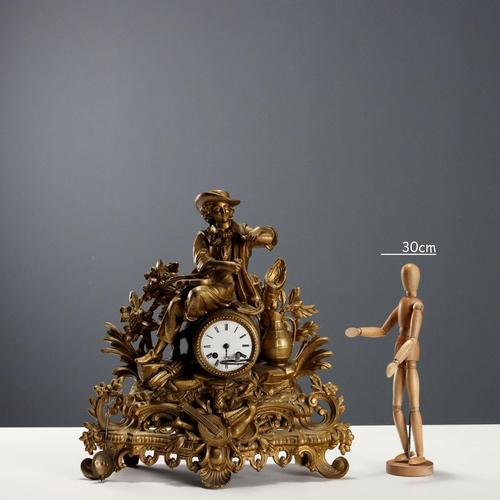 Gilded antimony table clock with a base decorated with plant motifs and a panoply of musical instruments. The clock is...