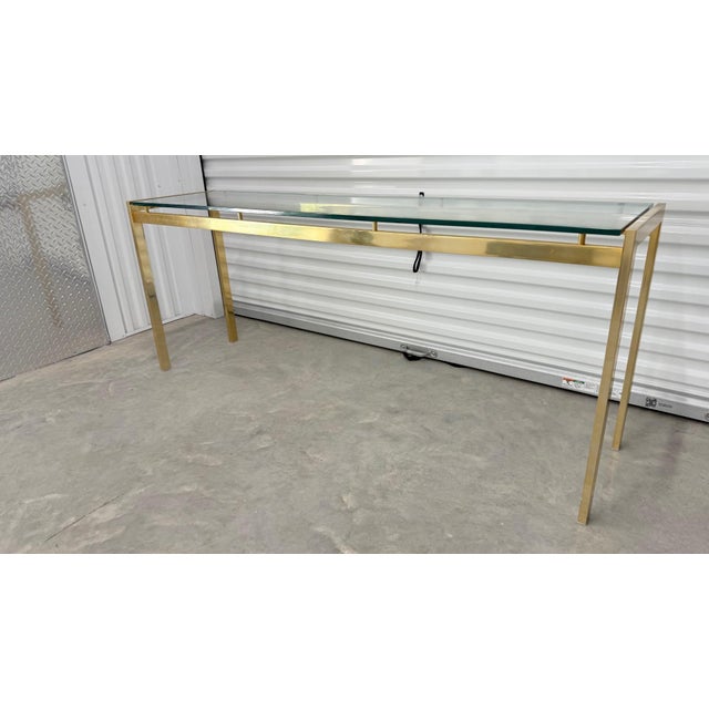 A refined vintage console table featuring a polished brass frame with a thick, beveled glass top that appears to float...
