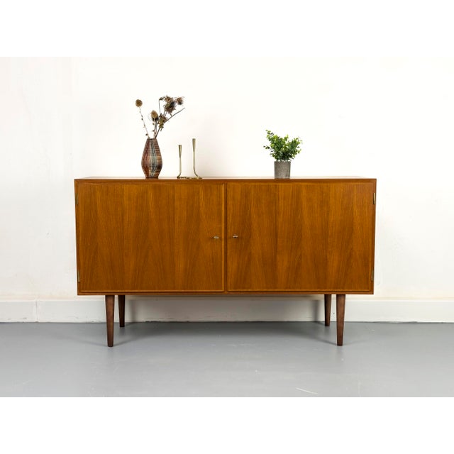 Compact and practical teak sideboard with two lockable cabinet doors. The interior is veneered in light maple and features...