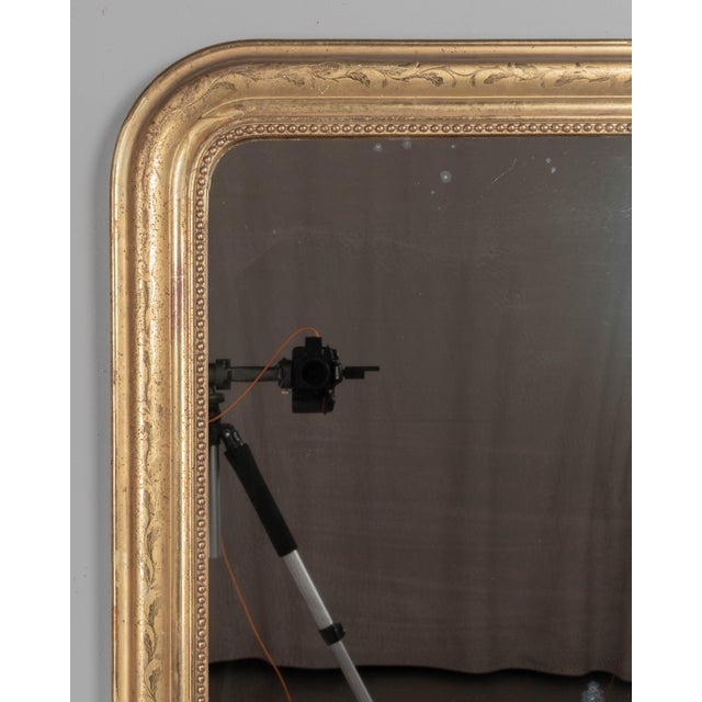 An early 20th century French Louis Philippe style gilded mirror with curved top corners, incised floral decoration and...