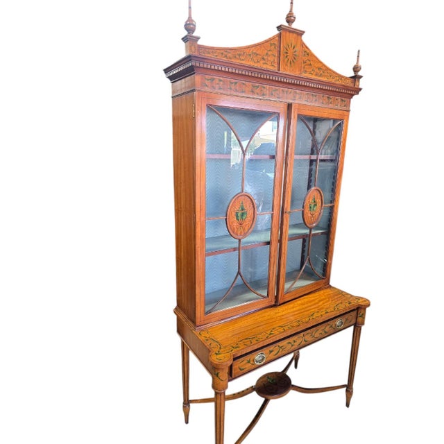 Elegant two-piece display cabinet featuring decorative glass-front doors, painted urn medallions, scrolling floral...