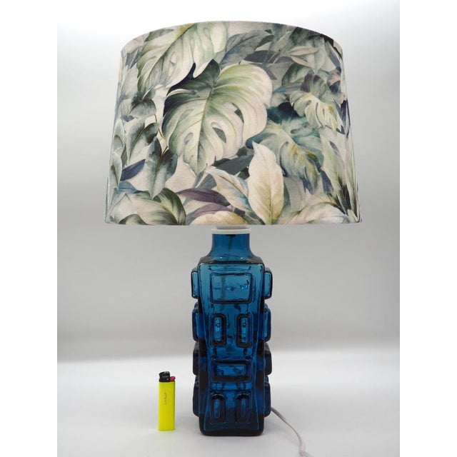 This unique table lamp combines a strong geometric glass base in deep cobalt blue with a lush lampshade in a botanical...