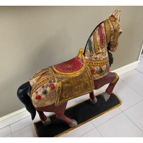 A large carved and painted wooden carousel style horse in a standing pose on a black base with vibrant polychrome...
