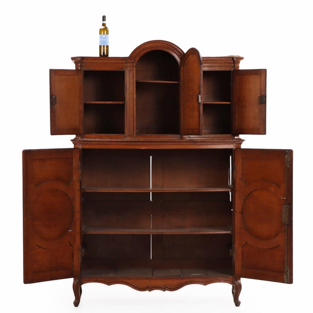 The upper section features a central arched cabinet door flanked by a pair of paneled doors, all enclosed within molded...
