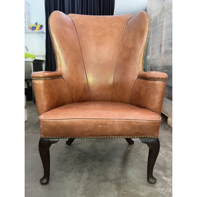 French Country wingback armchair, hand-crafted in the 20th Century. Beautifully tailored leather upholstery with brass...