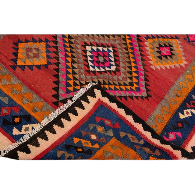 Beautiful vintage Turkish Kilim hand-knotted wool runner with a red field. This rug has a navy blue frame and multicolor...