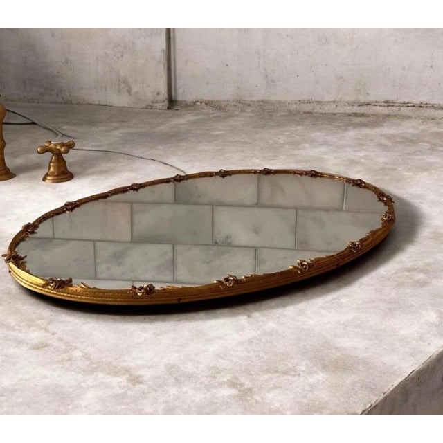 vintage Hollywood Regency-style gold-tone ornate oval mirrored vanity tray featuring decorative floral or filigree metal...