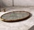 vintage Hollywood Regency-style gold-tone ornate oval mirrored vanity tray featuring decorative floral or filigree metal...