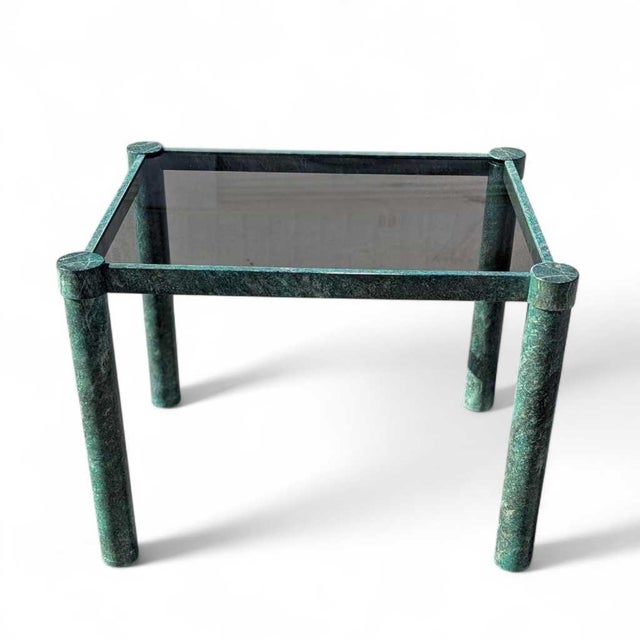 A compact 1980s postmodern side table with a smoked glass top and sculptural metal frame finished in a mottled green-gray...