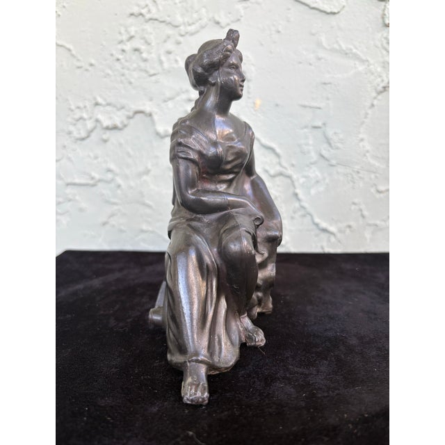 This antique decorative sculpture depicts a seated classical lady gently resting her hand on a harp, symbolizing music,...