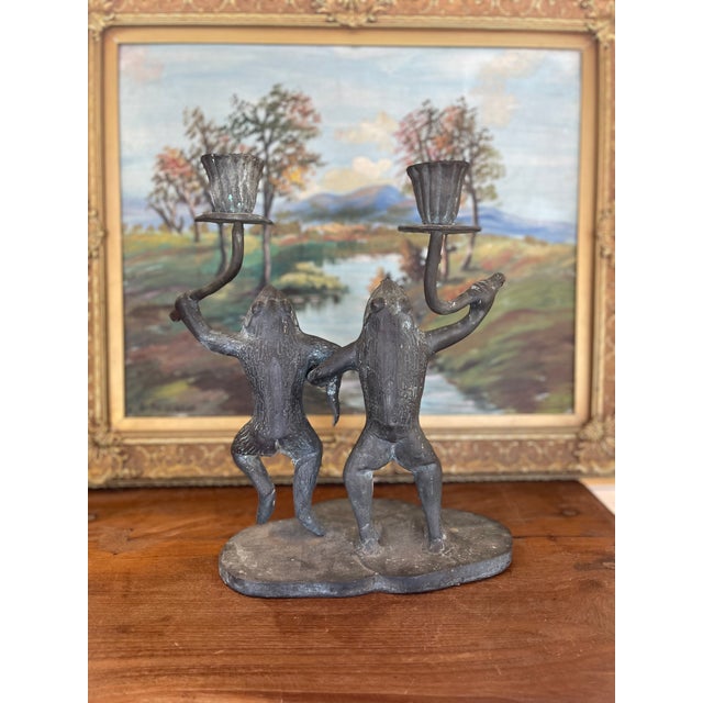 Playful and sculptural, this vintage candelabra features two anthropomorphic frogs captured mid-dance, each holding a...