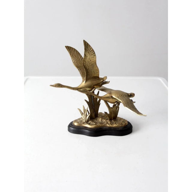 Vintage brass bird sculpture depicting two birds in flight over marshland grasses. The streamlined forms convey a sense of...