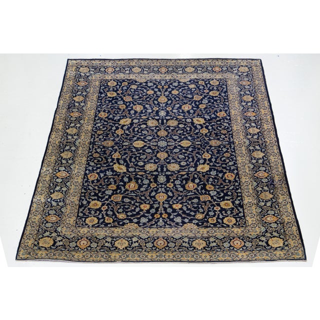 This Kashan Persian wool rug has a navy blue field with an allover floral pattern in yellow, beige, and light blue hues....