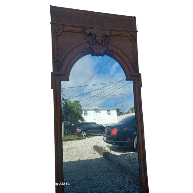 Vintage monumental French wooden Tremeau mirror. The mirror has a intricately carved wooden face and decorations. Back of...