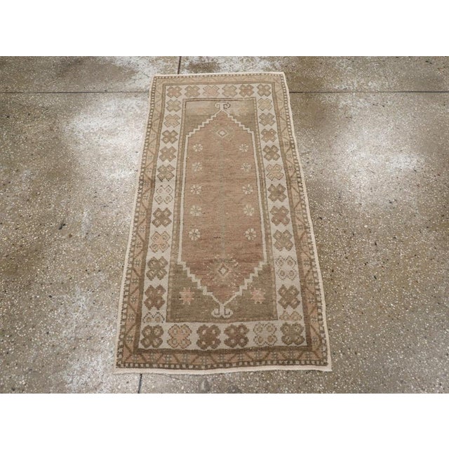 A vintage Turkish Oushak throw rug. This narrow rustic scatter has a medium brown field with a sparse decoration of a...
