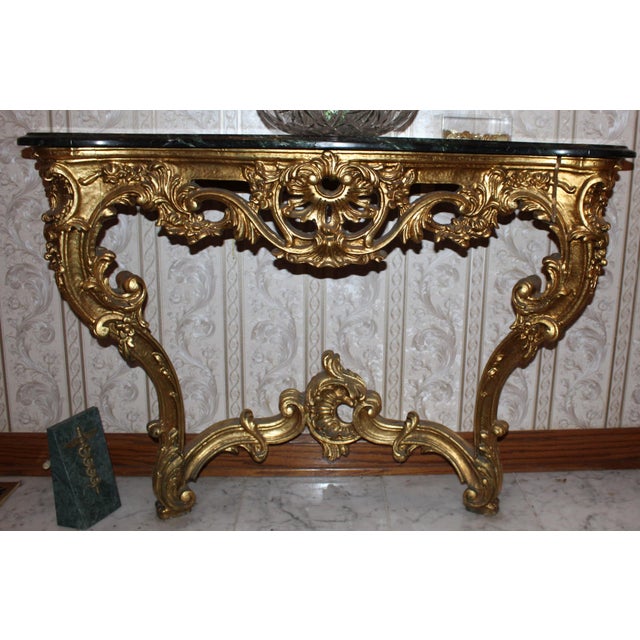 A Louis XV style wall console with a richly worked gilt frame beneath a serpentine dark green marble top veined in white....
