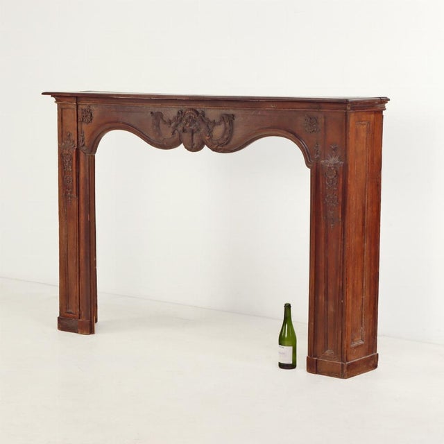 An elegant 18th-century French fireplace mantel, finely carved from solid oak. The shaped apron is adorned with delicate...
