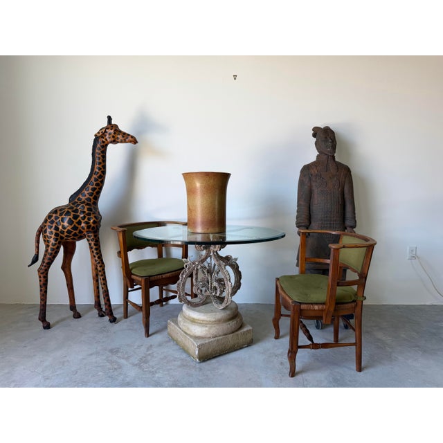 Striking vintage outdoor dining table featuring an ornate wrought iron pedestal base with beautifully scrolled detailing...
