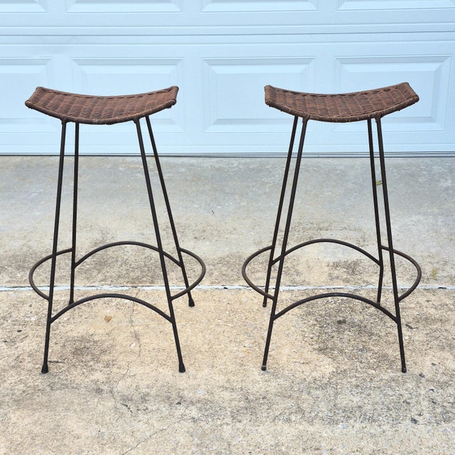 This is a stylish pair of midcentury modern bar height stools featuring handwoven natural rattan tops supported by sleek...