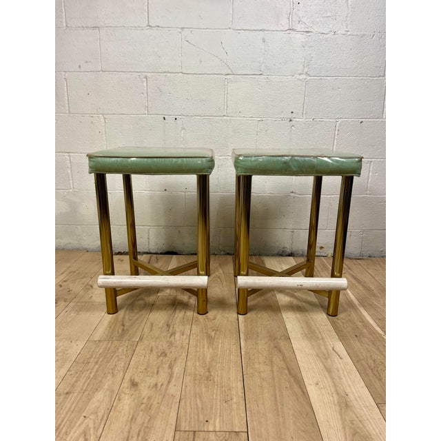 Glamorous pair of vintage Hollywood Regency bar stools dating to the 1970s. Each stool features a polished tubular brass...