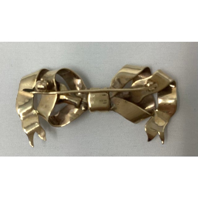 Artfully tied 14k yellow gold pin in the shape of a ribbon. Tests 14k