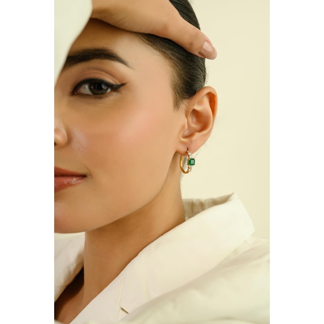 These Dainty Hoop Earrings features 2 square cut emeralds totaling 1.45 carats, set in rich 18K Solid Yellow Gold. The...