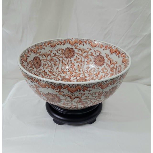 Large Chinese porcelain punch bowl featuring an intricate all-over floral and vine motif in a warm burnt orange and...