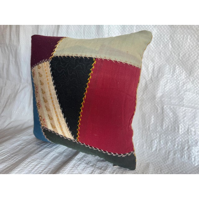 This vintage American patchwork pillow features a hand-stitched composition of repurposed fabric panels, each arranged in...
