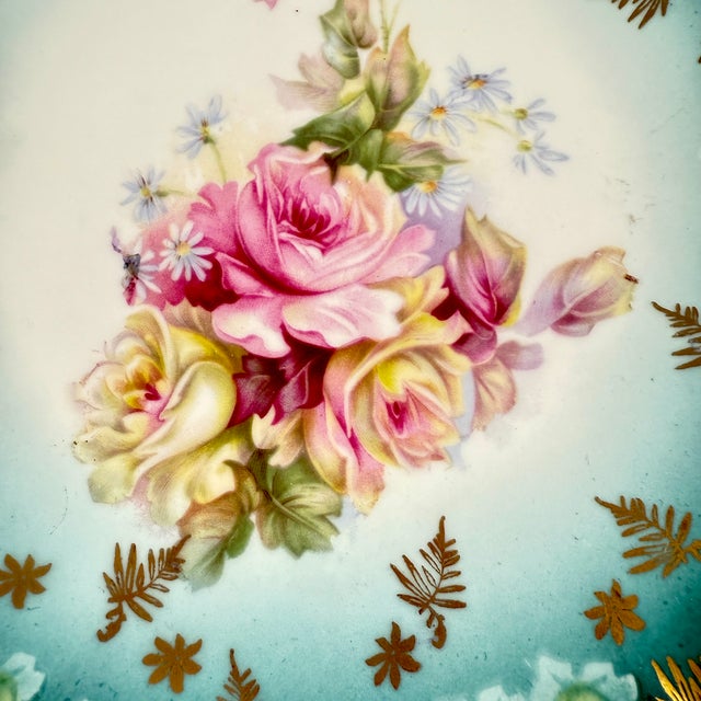 A deep porcelain plate with pink roses and a gilded leaf border, Bohemia, circa 1900. A rich Teal blue ground fading...