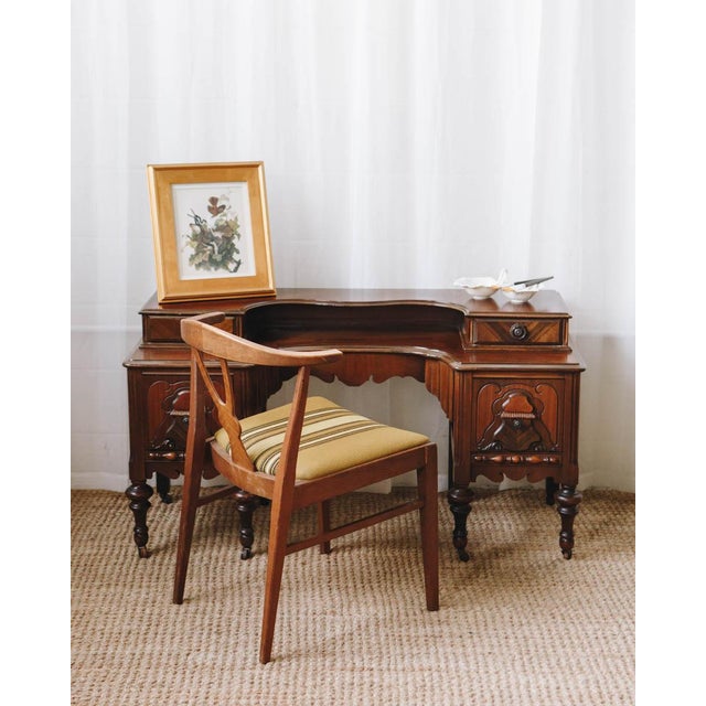 An elegant early 20th century vanity desk, crafted in richly toned wood with beautifully detailed carving and a graceful,...
