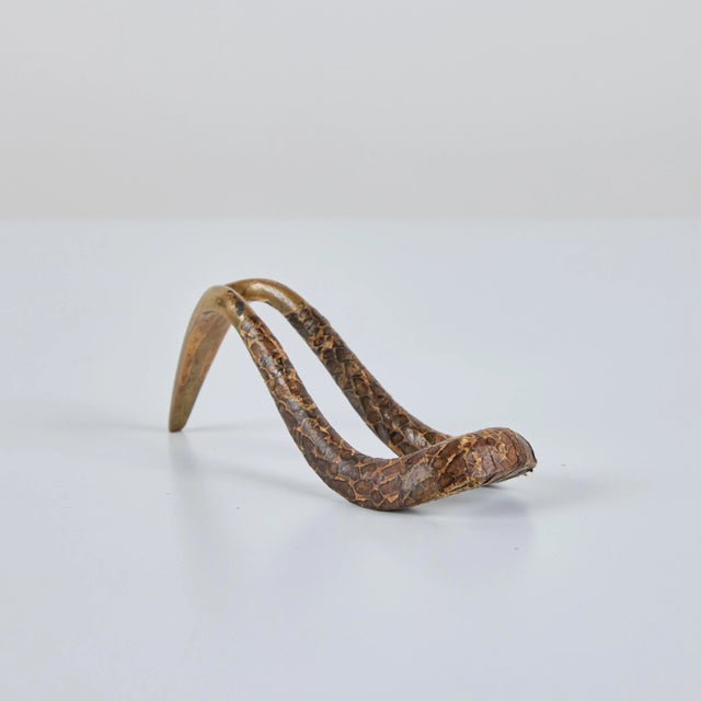 Brass and snakeskin pipe stand by Austrian industrial designer Carl Auböck, c.1950s. The curved brass frame is partially...