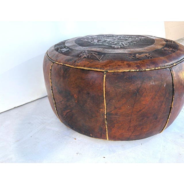 Vintage Brown Tooled Saddle Leather Peruvian Ottoman Hassock. Item features an intricate embossed figure at the center,...