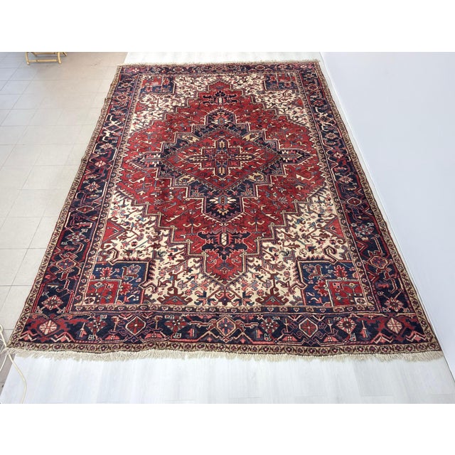 8’ 6” x 11’ 5” Vintage Persian Heriz room size rug from the mid 1900s in a red and ivory color background with the central...