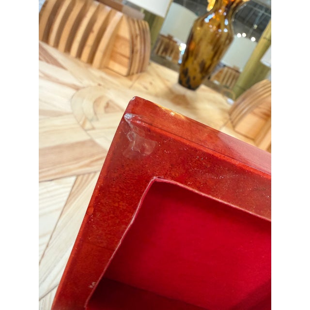 A striking red lacquered box featuring a glossy, high-shine finish in a warm coral-red tone with natural mottled variation...