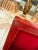 A striking red lacquered box featuring a glossy, high-shine finish in a warm coral-red tone with natural mottled variation...